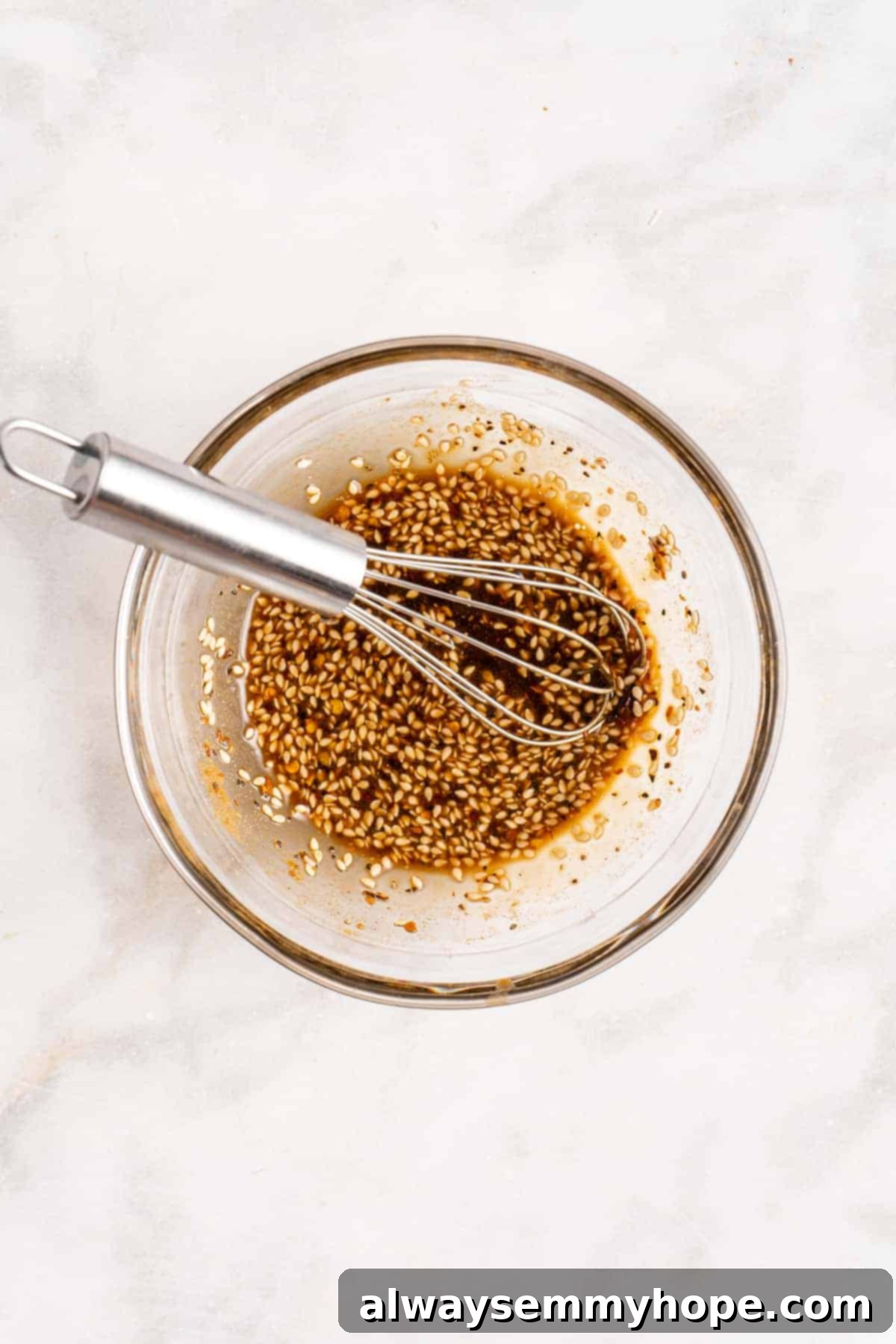 Step-by-step instructions on how to make vegan potstickers at home! These Chinese dumplings are filled with tofu and veggies. So good! Overhead view of a small glass bowl filled with the vibrant sweet ginger dipping sauce, accompanied by a whisk and garnishes like sesame seeds and chopped green onions.