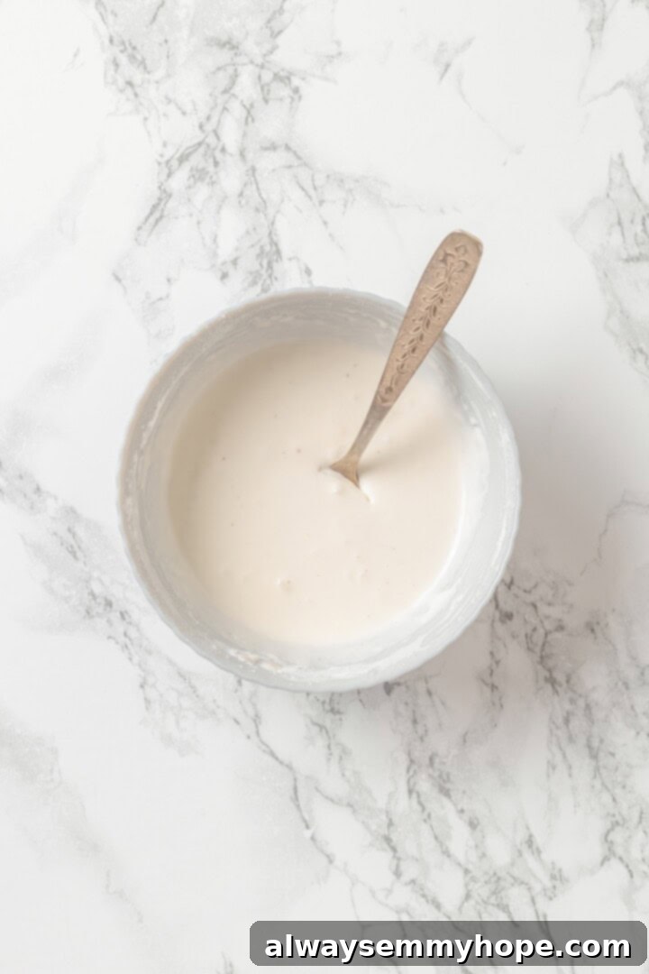 A small bowl showing cornstarch being whisked into coconut cream until smooth.