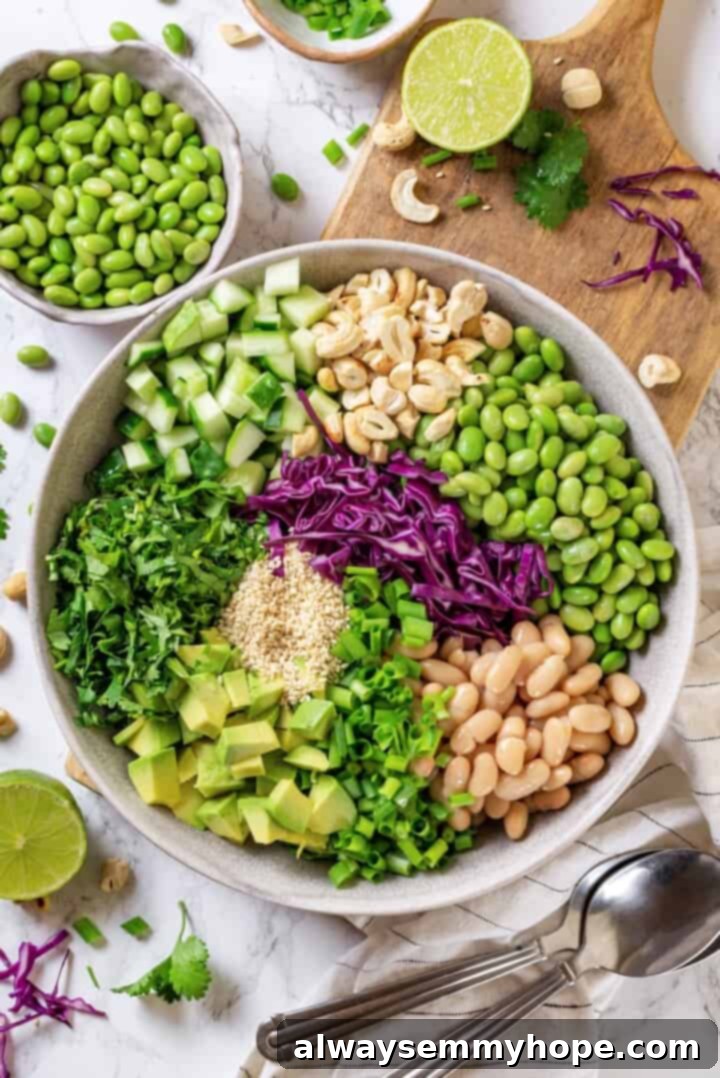 Overhead view of various edamame salad ingredients, including edamame, cucumber, red cabbage, and green onions, mixed in a large bowl before dressing.