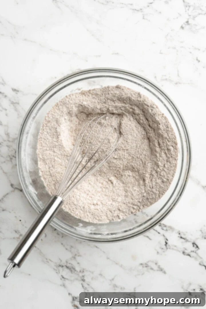Overhead view of a flour mixture in a mixing bowl with a whisk, perfectly combined and ready for wet ingredients.