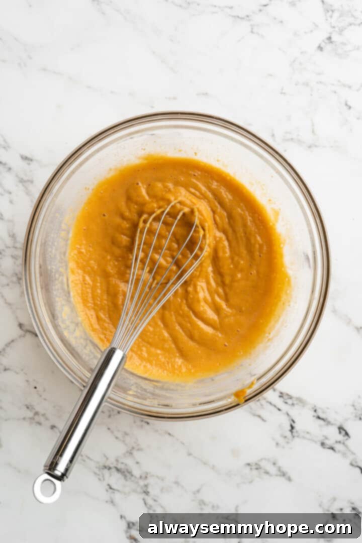 Overhead view of a smooth pumpkin puree mixture in a mixing bowl with a whisk, showing the liquid ingredients blended.