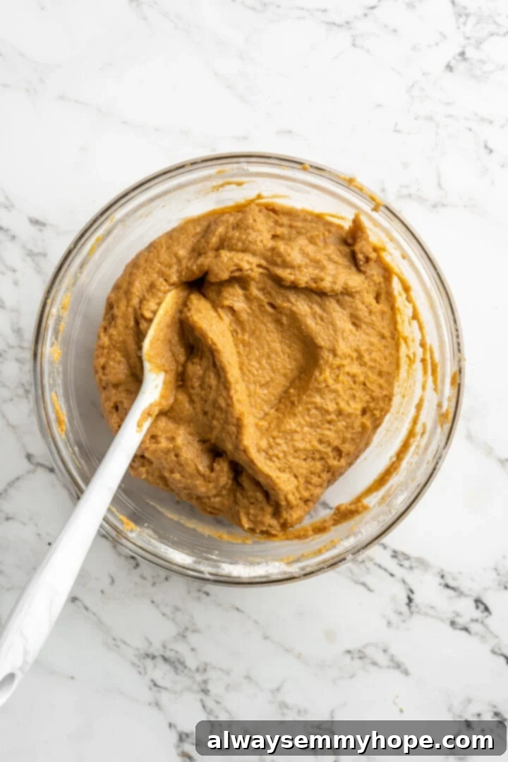 Overhead view of thick pumpkin muffin batter in a mixing bowl with a spatula, perfectly mixed and ready for chocolate chips.
