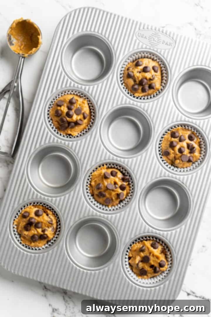 Overhead view of a muffin tray with six muffin tins filled with raw pumpkin chocolate chip batter, ready for baking.