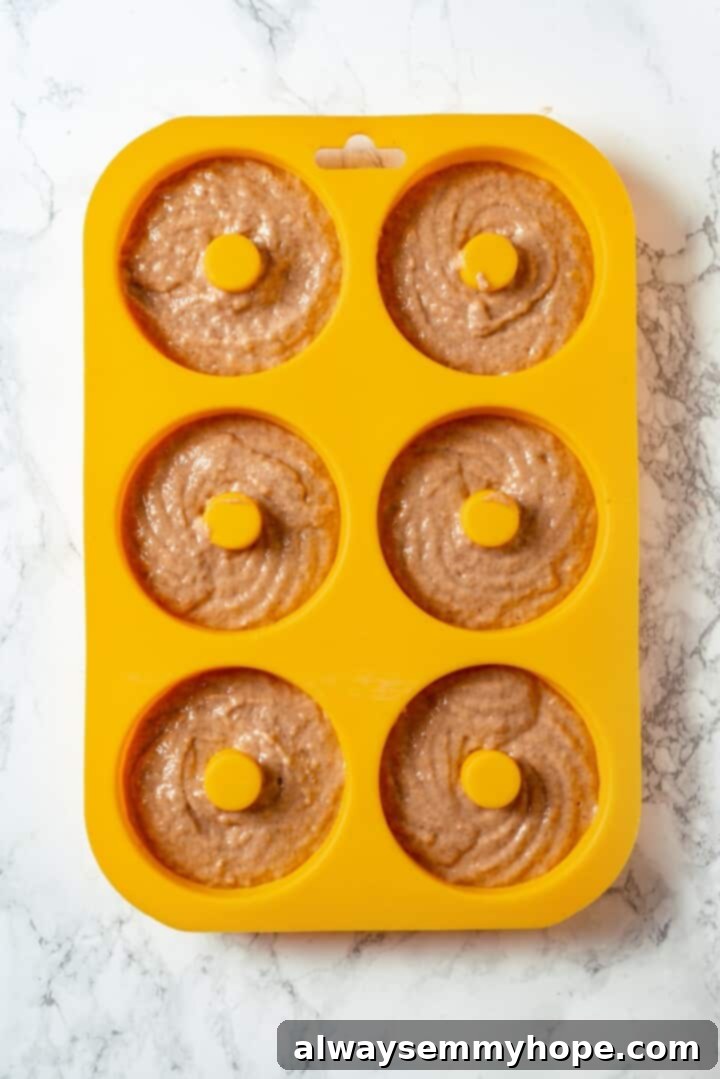 These tender cinnamon-spiced Apple Cider Donuts are baked instead of fried and made without yeast, which means they're super easy to make! Batter for apple cider donuts in silicone pan.