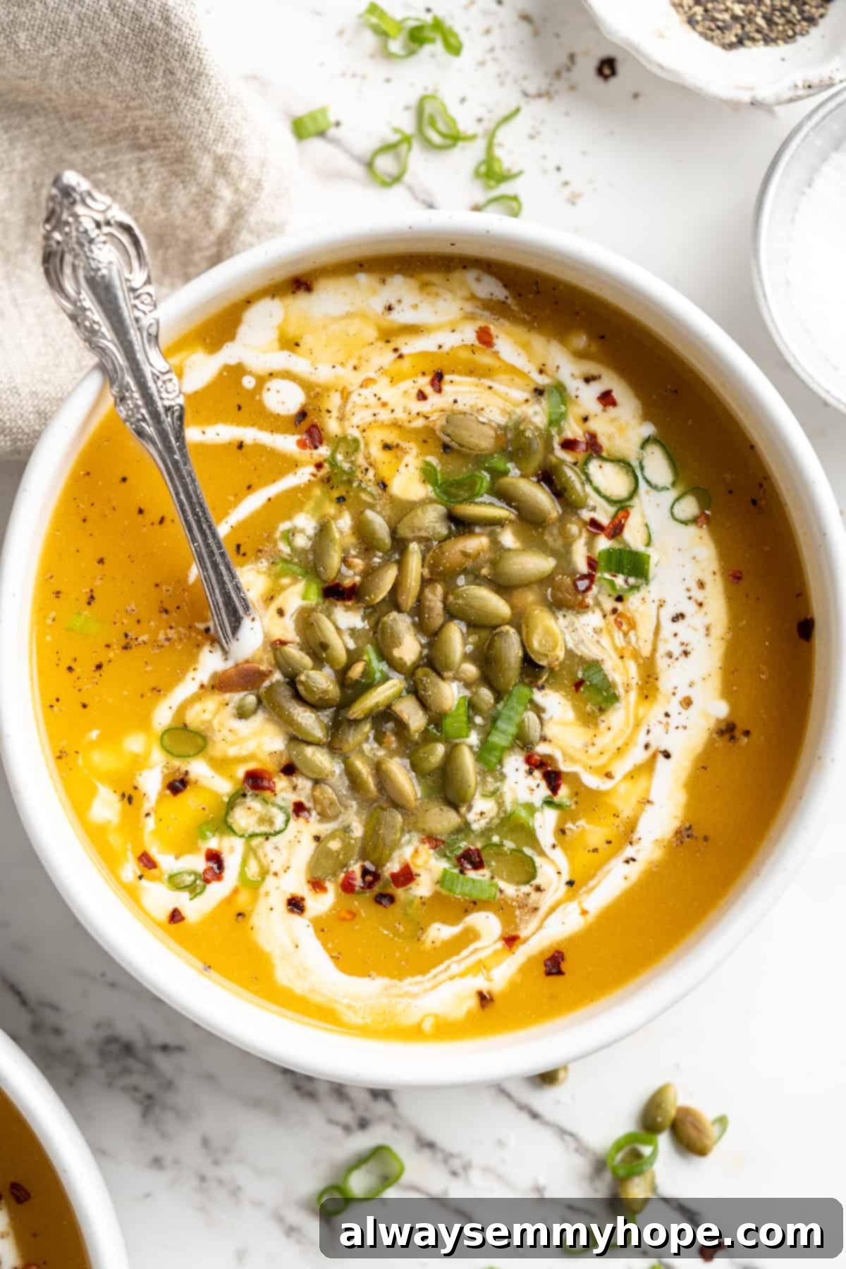 Overhead view of pumpkin soup in bowl with spoon and pepitas, green onions, and coconut cream garnish