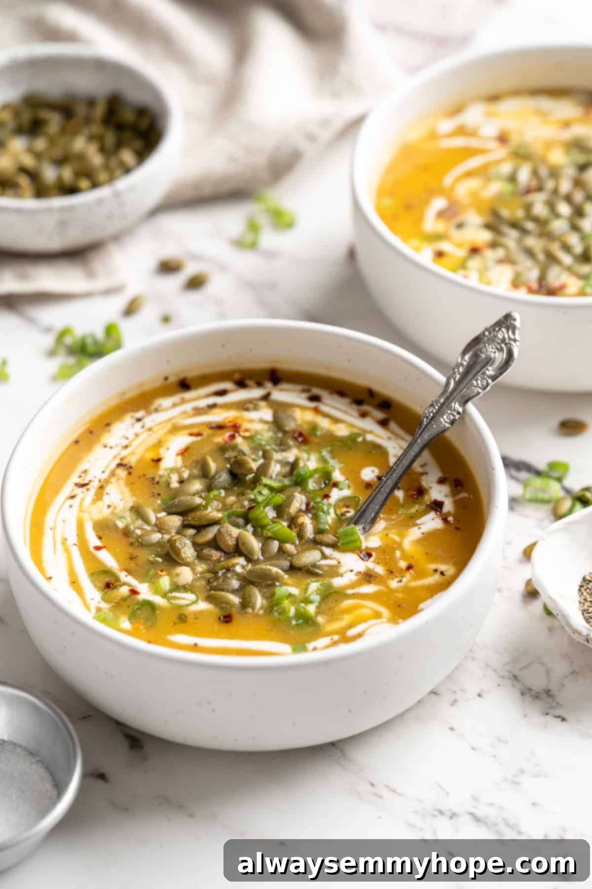 Creamy pumpkin soup in white bowls with pepitas, green onions, and coconut cream garnish