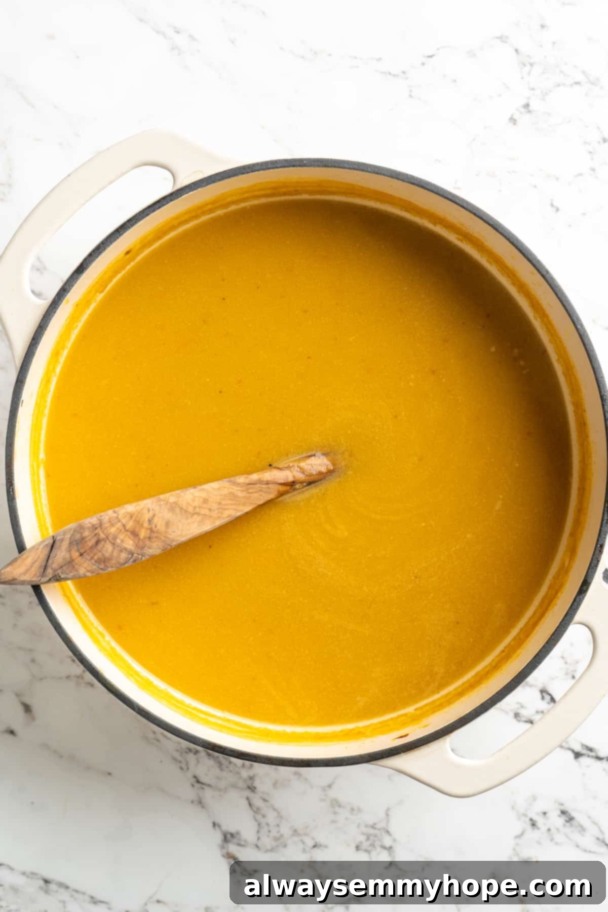 Overhead view of pureed pumpkin soup in pot with wooden spoon