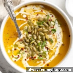 Overhead view of pumpkin soup in bowl with spoon and pepitas, green onions, and coconut cream garnish