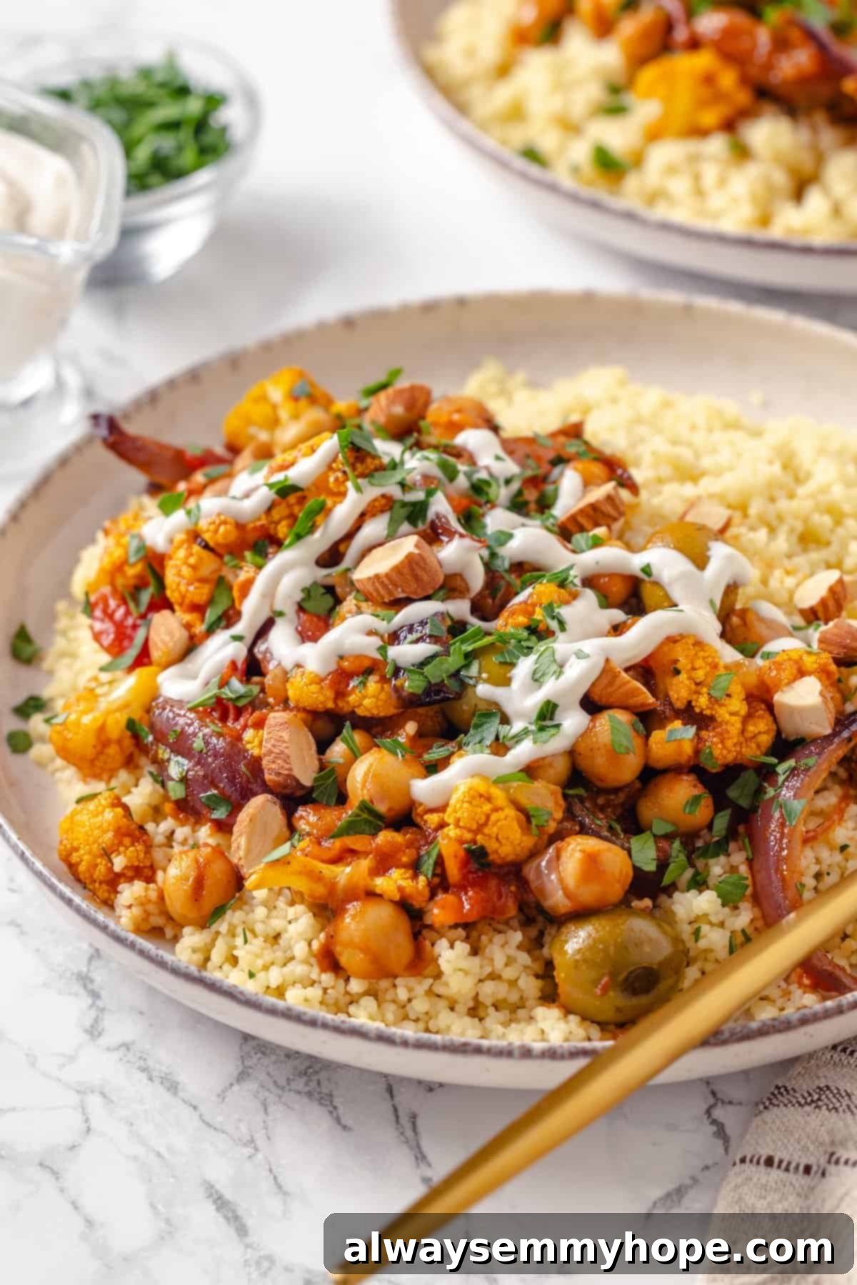 Warm spices mingle with vegetables, golden raisins, olives and chickpeas to make this Moroccan Cauliflower Tagine a delicious vegan dinner! Bowl with Moroccan cauliflower tagine and couscous.