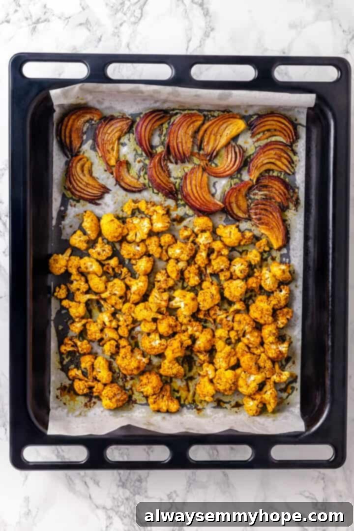 Warm spices mingle with vegetables, golden raisins, olives and chickpeas to make this Moroccan Cauliflower Tagine a delicious vegan dinner! Roasted red onions and cauliflower in pan.