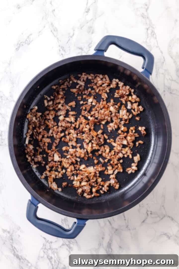 Warm spices mingle with vegetables, golden raisins, olives and chickpeas to make this Moroccan Cauliflower Tagine a delicious vegan dinner! Onions, garlic, and spices cooking in pan.