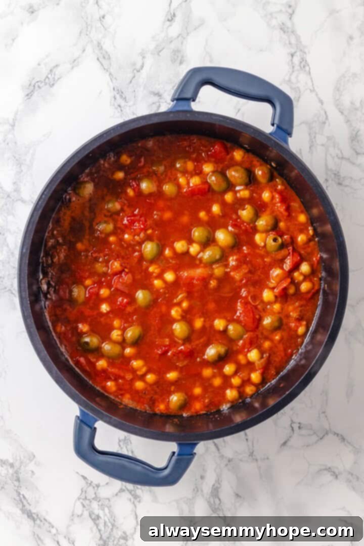 Warm spices mingle with vegetables, golden raisins, olives and chickpeas to make this Moroccan Cauliflower Tagine a delicious vegan dinner! Sauce for Moroccan cauliflower tagine in pan.