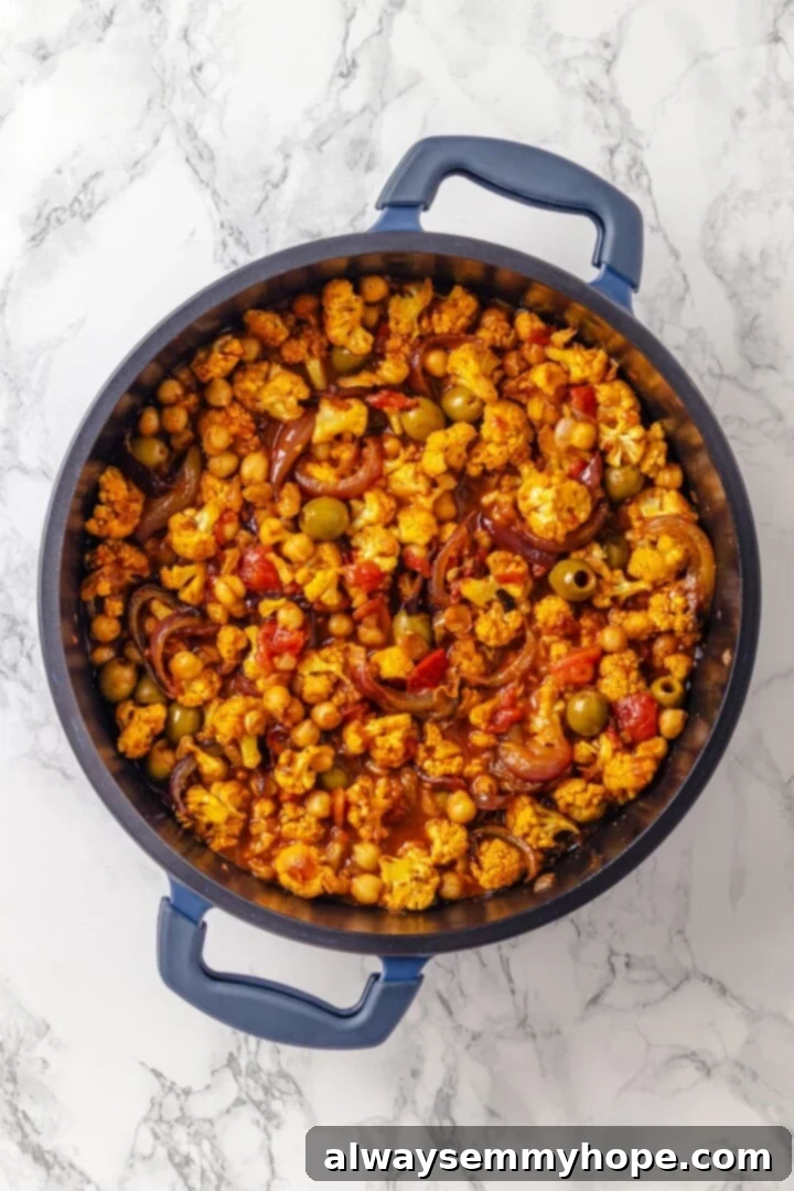 Warm spices mingle with vegetables, golden raisins, olives and chickpeas to make this Moroccan Cauliflower Tagine a delicious vegan dinner! Moroccan cauliflower tagine in skillet.