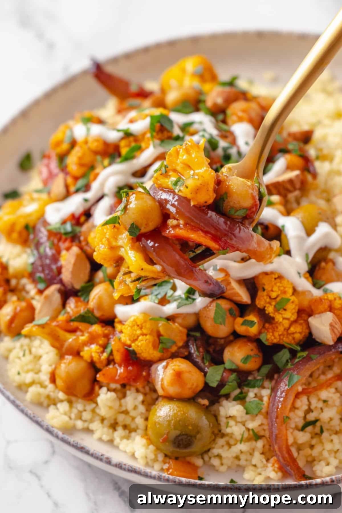 Warm spices mingle with vegetables, golden raisins, olives and chickpeas to make this Moroccan Cauliflower Tagine a delicious vegan dinner! Forkful of Moroccan cauliflower tagine held over bowl.