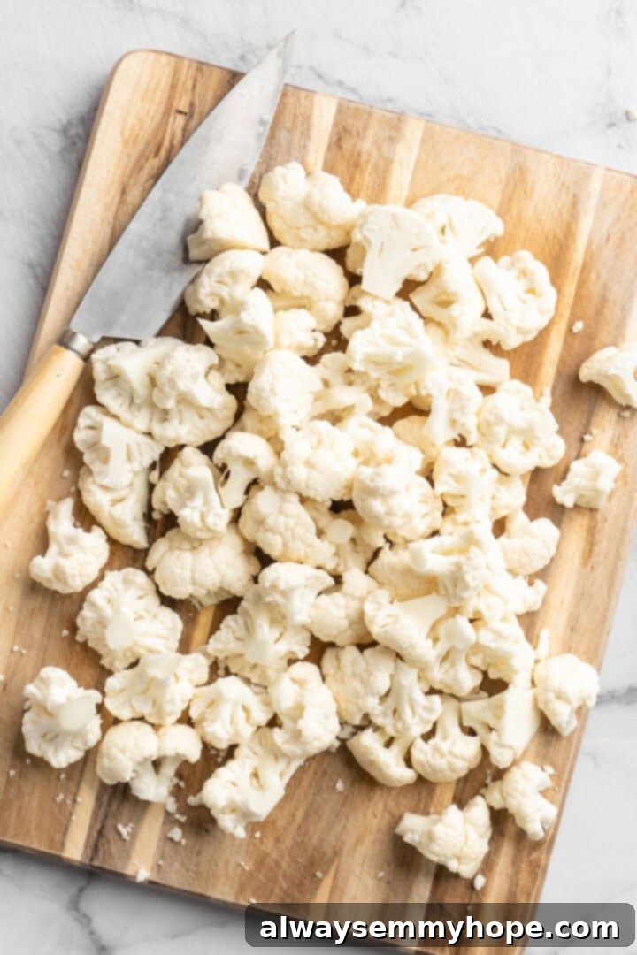 These Cauliflower Bites are crispy, crunchy and full of big flavour thanks to an irresistible sweet sriracha sauce. A total crowd pleaser! Overhead view of a head of cauliflower being cut into uniform florets on a wooden cutting board with a chef's knife
