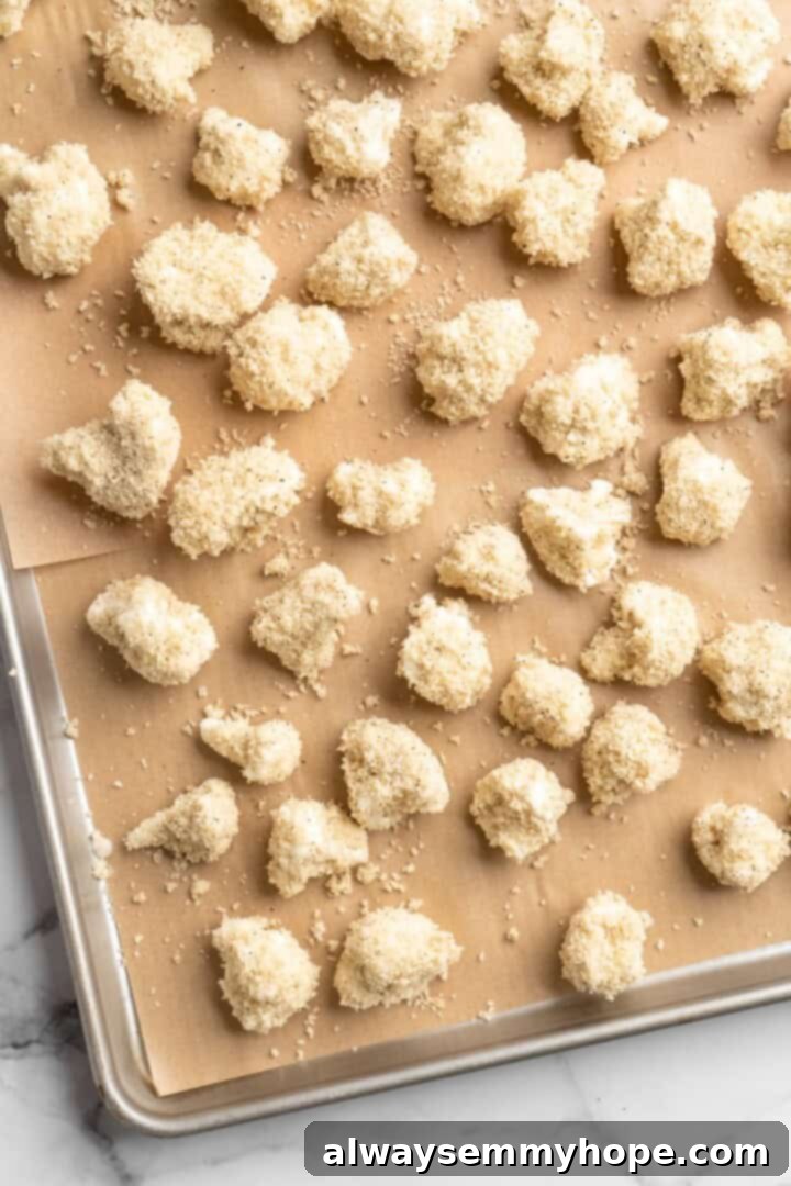 These Cauliflower Bites are crispy, crunchy and full of big flavour thanks to an irresistible sweet sriracha sauce. A total crowd pleaser! Overhead view of unbaked, breaded cauliflower bites spread evenly on a sheet pan, ready for the oven
