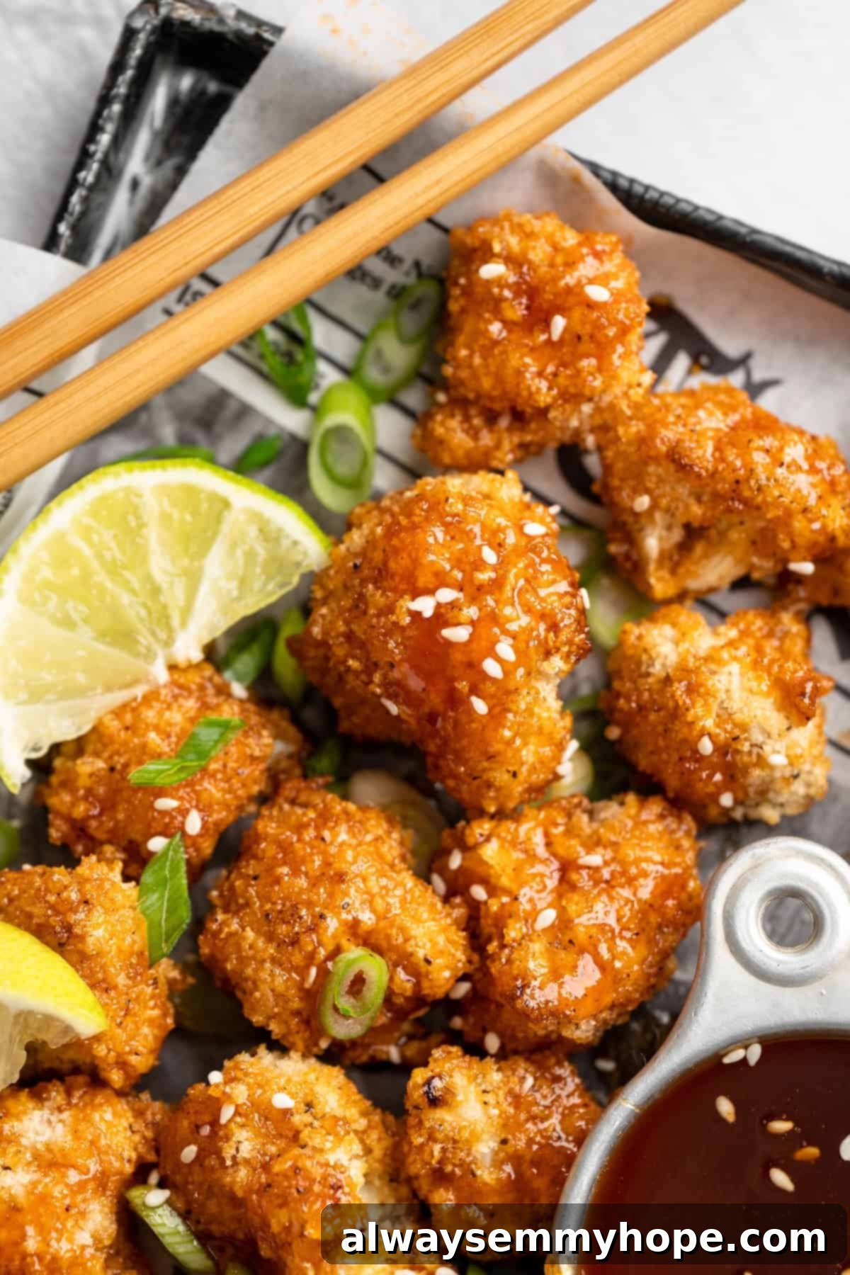 These Cauliflower Bites are crispy, crunchy and full of big flavour thanks to an irresistible sweet sriracha sauce. A total crowd pleaser! Sheet pan filled with crispy sweet sriracha cauliflower bites, with a bowl of dipping sauce, chopsticks, and a lime wedge