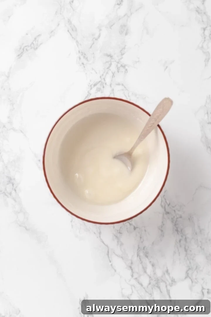 Tender apples, sticky glaze, and dough that’s crisp on the outside and pillowy soft inside make this the best vegan apple fritters recipe! Small bowl of smooth vanilla glaze with a spoon.