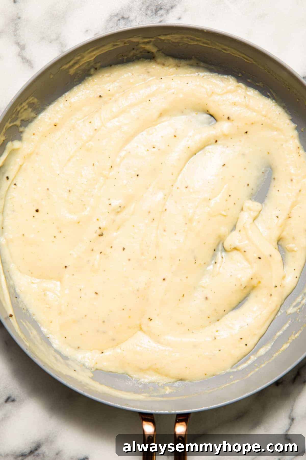 A creamy white sauce being prepared in a pan with coconut flour and vegan milk.