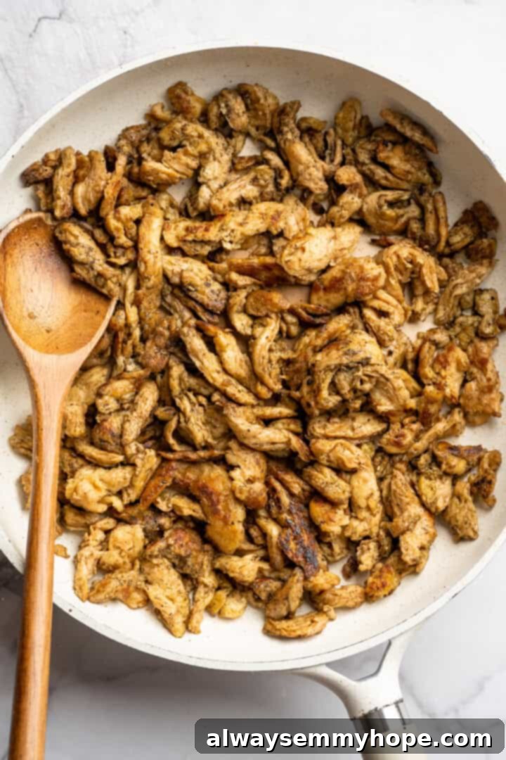 Vegan chicken in skillet with wooden spoon.