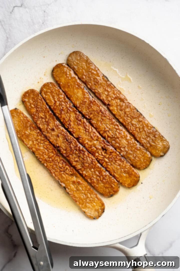 Tempeh bacon cooking in skillet.