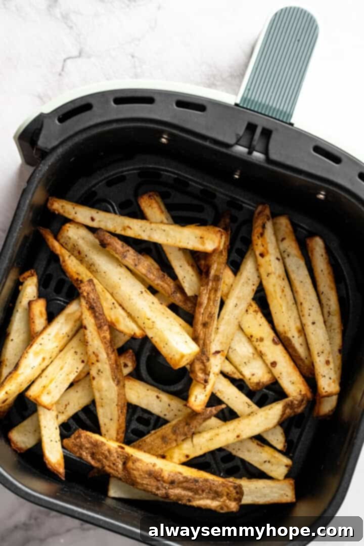 Air frying the potato wedges until golden brown and crispy. French fries in air fryer basket.
