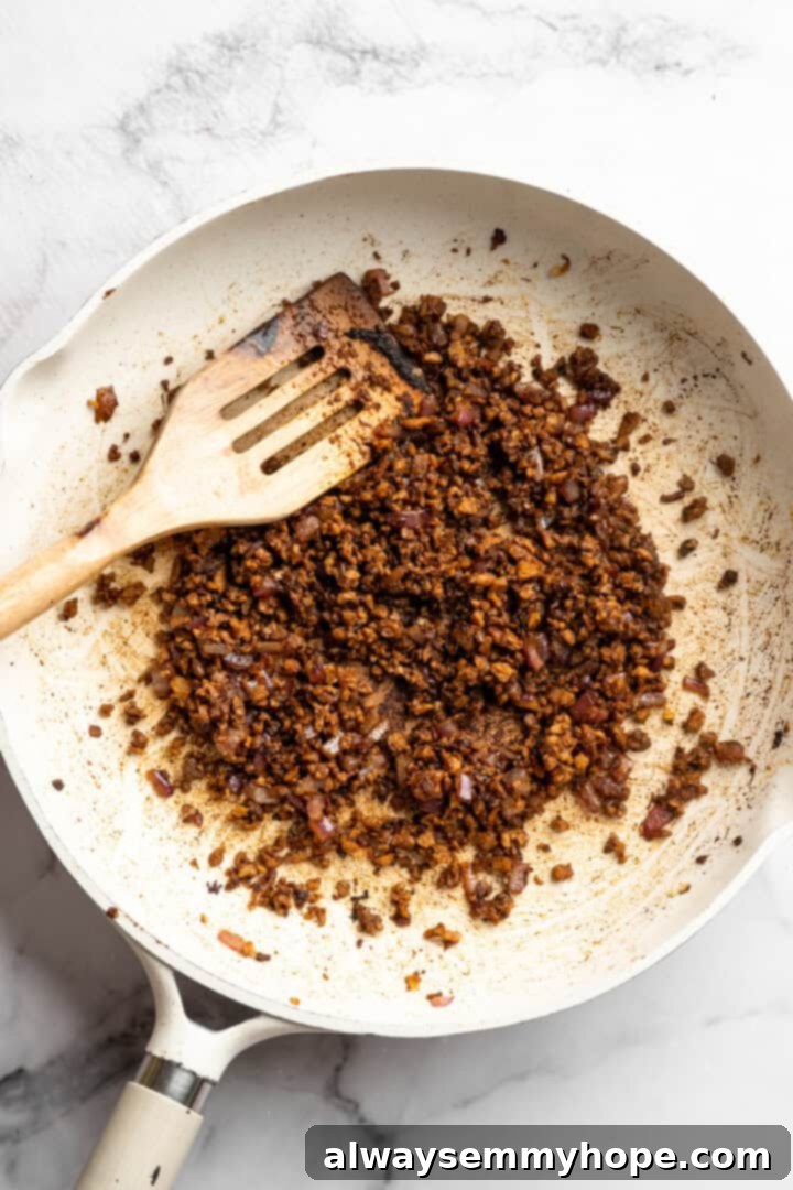 Cooking the TVP (Textured Vegetable Protein) with onions and spices for a flavorful burger crumble. TVP cooking in skillet.