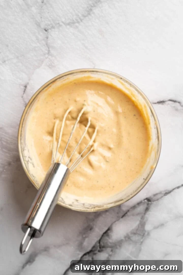 Whisking together the ingredients for a creamy and tangy vegan burger sauce. Burger sauce in bowl with whisk.