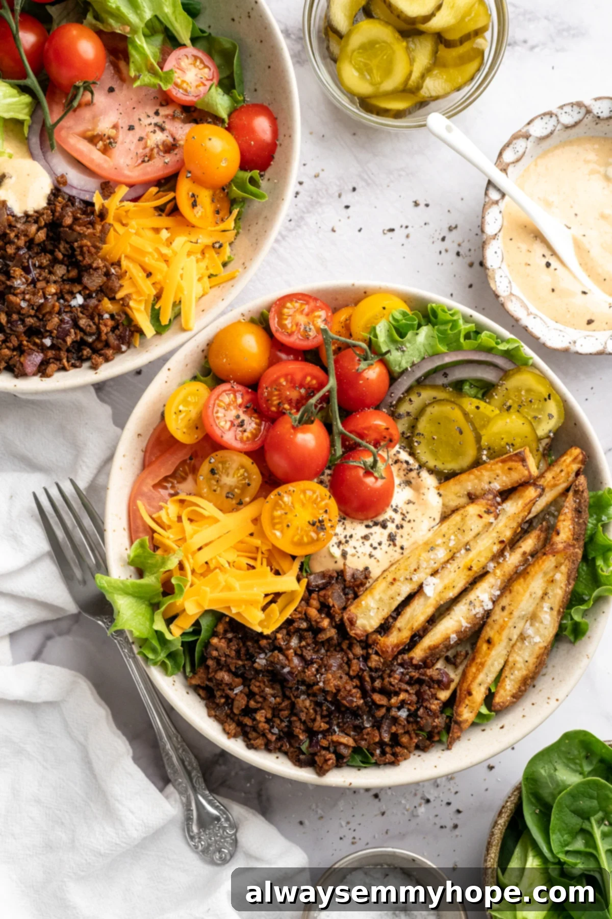 Two delicious and colorful Vegan Cheeseburger Bowls ready to be enjoyed. Two vegan cheeseburger bowls with tomatoes, fries, pickles, and other toppings.