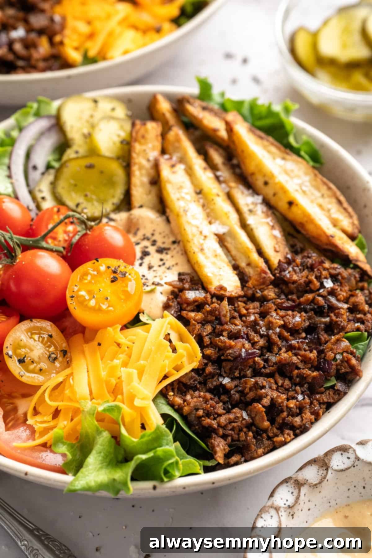 A perfectly assembled Vegan Cheeseburger Bowl with fries, sauce, and all the fixings. Vegan cheeseburger bowl with fries.
