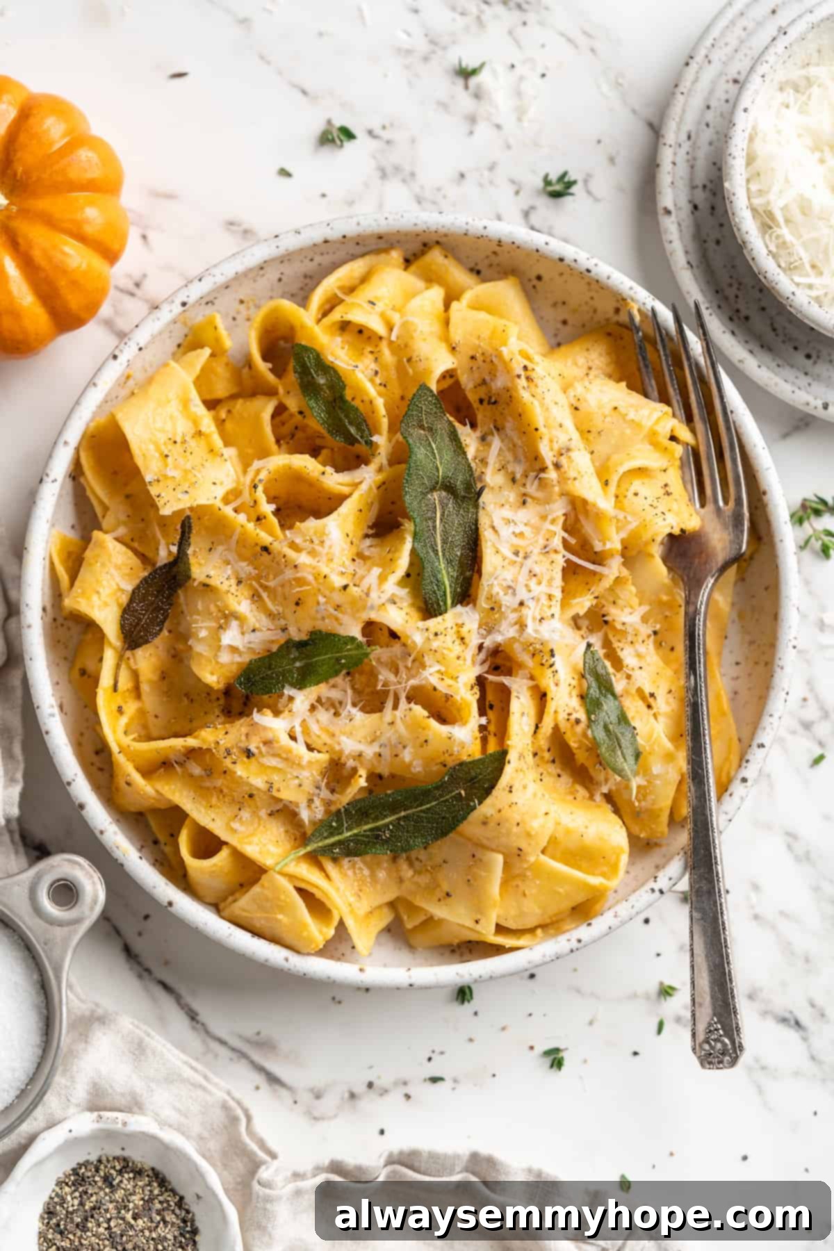 This easy pumpkin Alfredo pasta is rich, creamy, and perfect for a weeknight. Turn simple pantry ingredients into a restaurant-style meal! Overhead view of pumpkin alfredo pasta in bowl with fork and crispy sage leaf garnish