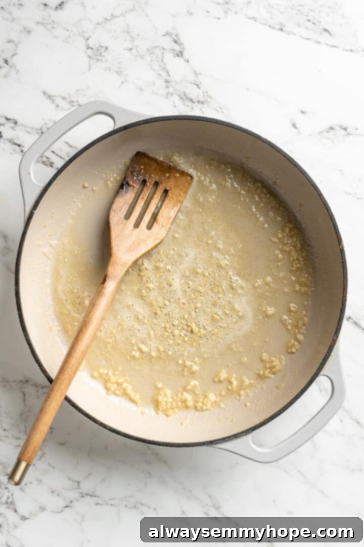 This easy pumpkin Alfredo pasta is rich, creamy, and perfect for a weeknight. Turn simple pantry ingredients into a restaurant-style meal! Overhead view of butter and garlic in skillet with wooden spoon