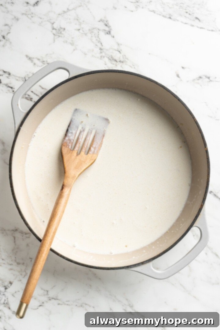 This easy pumpkin Alfredo pasta is rich, creamy, and perfect for a weeknight. Turn simple pantry ingredients into a restaurant-style meal! Overhead view of cream poured into skillet with wooden spoon