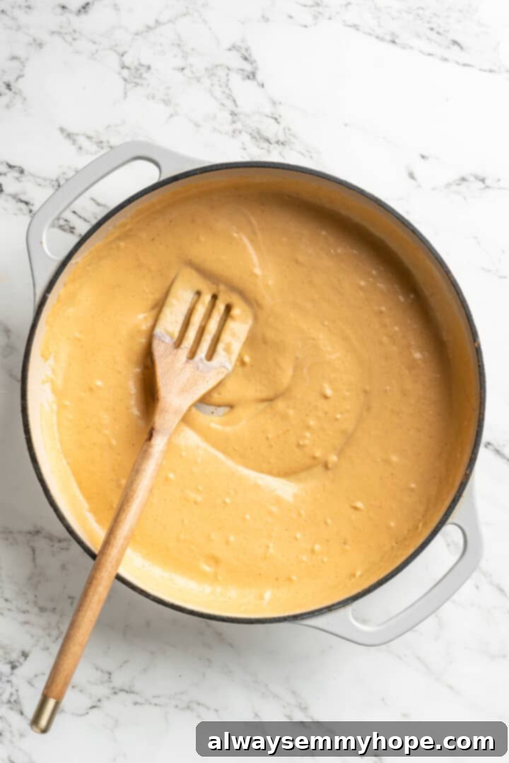 This easy pumpkin Alfredo pasta is rich, creamy, and perfect for a weeknight. Turn simple pantry ingredients into a restaurant-style meal! Overhead view of wooden spoon stirring skillet of pumpkin alfredo sauce
