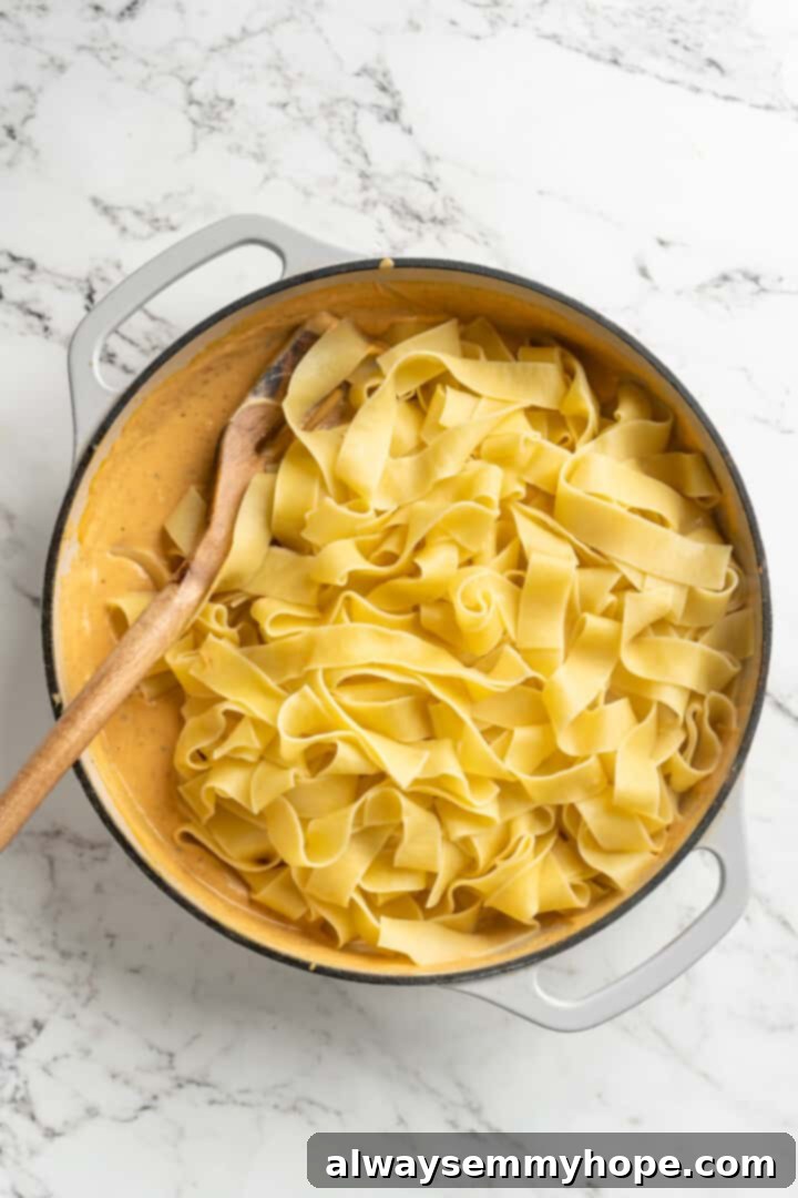 This easy pumpkin Alfredo pasta is rich, creamy, and perfect for a weeknight. Turn simple pantry ingredients into a restaurant-style meal! Overhead view of fettuccine noodles added to skillet of creamy pumpkin sauce