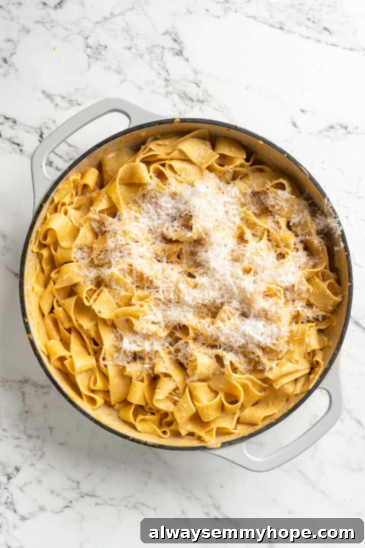 This easy pumpkin Alfredo pasta is rich, creamy, and perfect for a weeknight. Turn simple pantry ingredients into a restaurant-style meal! Overhead view of vegan parmesan cheese added to skillet of pumpkin alfredo pasta