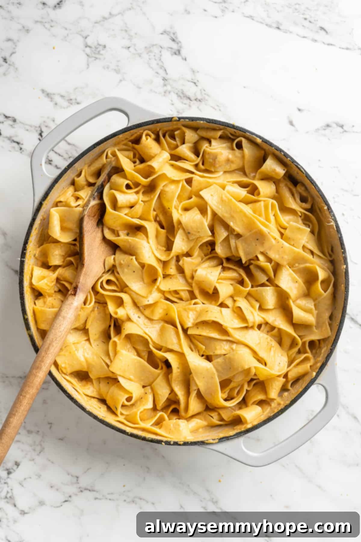 This easy pumpkin Alfredo pasta is rich, creamy, and perfect for a weeknight. Turn simple pantry ingredients into a restaurant-style meal! Overhead view of fettuccine noodles in skillet being stirred with creamy pumpkin sauce