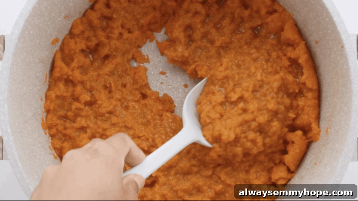 Maple Pecan Crunch Vegan Sweet Potato Bake 7 A spoon smoothly spreading the mashed sweet potato mixture into a glass casserole dish, creating an even base for the topping.