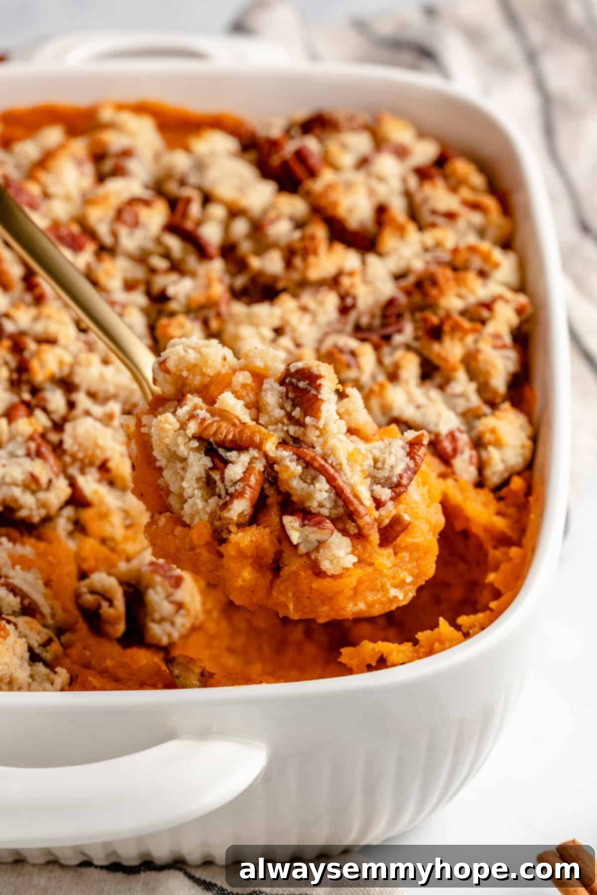 Maple Pecan Crunch Vegan Sweet Potato Bake 10 A close-up of a golden spoon scooping a fluffy portion of baked Vegan Sweet Potato Casserole from a white baking dish, showing off its perfectly browned maple pecan topping.