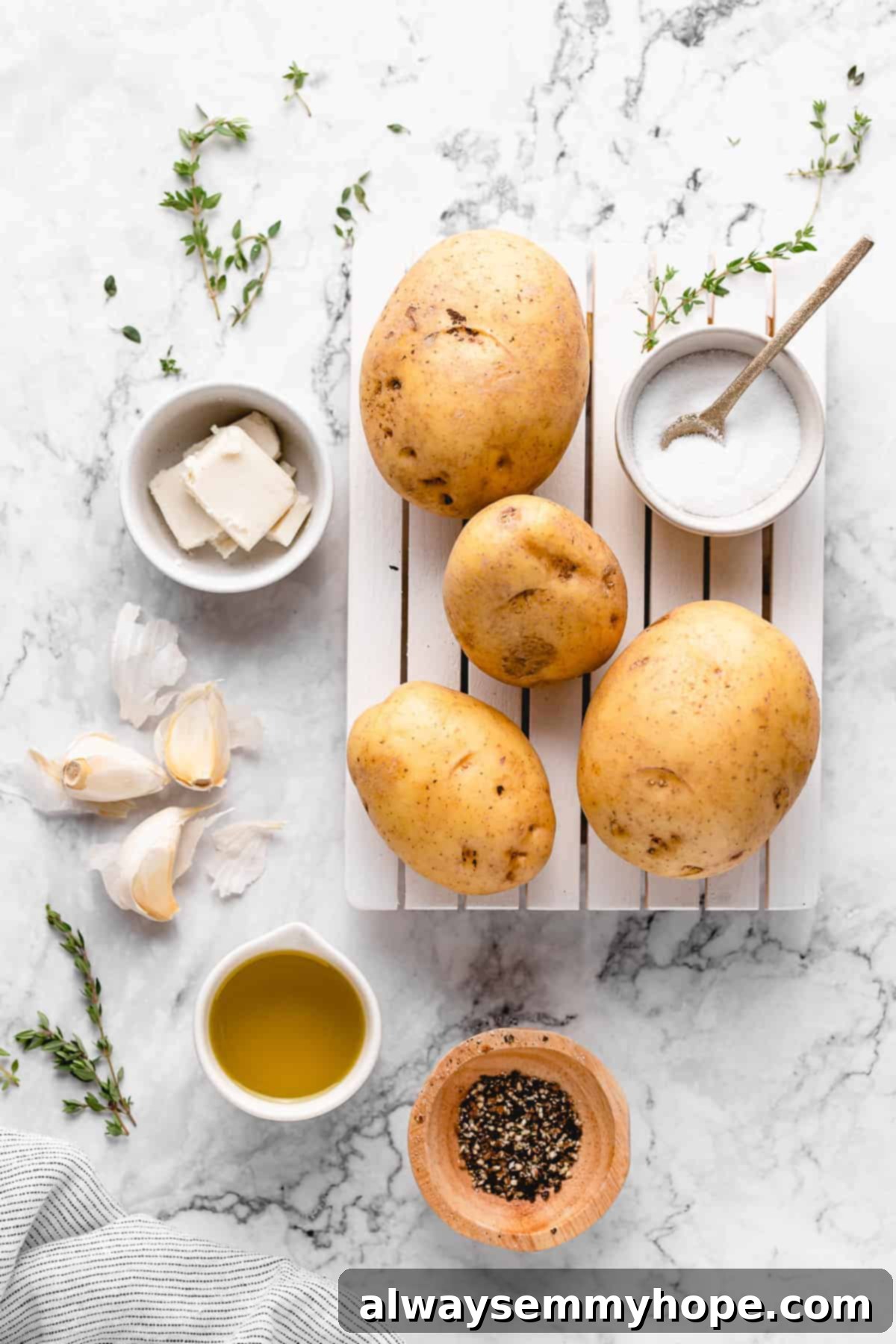 These garlic roasted potatoes are crispy, buttery and so tasty! They make a quick and easy side dish that goes with just about anything. A vibrant selection of fresh ingredients laid out on a clean counter, including raw potatoes, whole garlic cloves, fresh thyme sprigs, and bottles of olive oil and vegan butter, all ready for making garlic roasted potatoes.