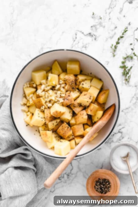 These garlic roasted potatoes are crispy, buttery and so tasty! They make a quick and easy side dish that goes with just about anything. Chopped potatoes, olive oil, salt, pepper, and large garlic pieces in a mixing bowl, ready to be tossed and seasoned.