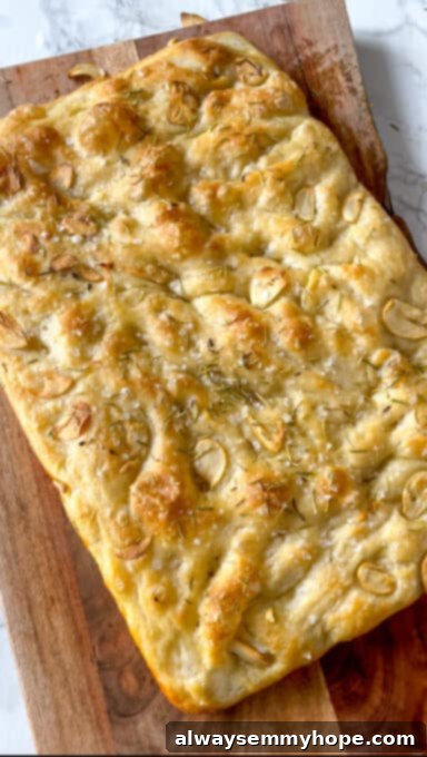A baked golden-brown focaccia bread on a wooden cutting board, ready to be sliced and served.