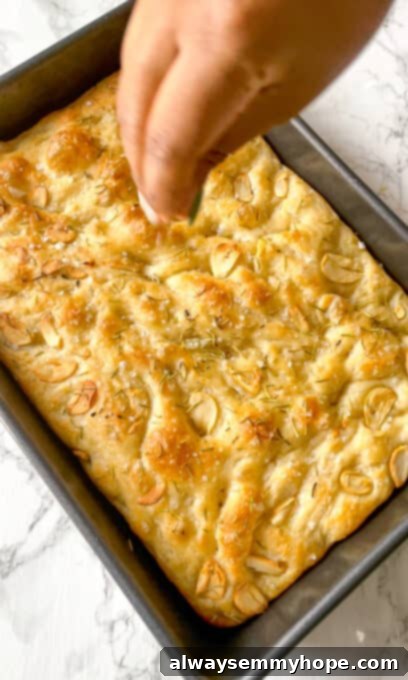 A hand sprinkling coarse sea salt over a warm, baked focaccia bread, enhancing its flavor and appearance.