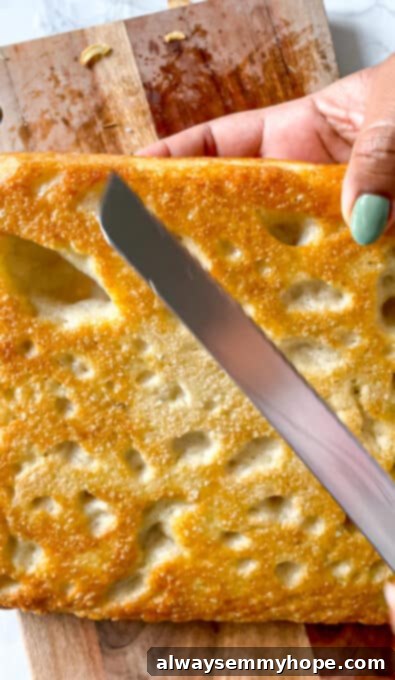 A knife positioned at the edge of a baked focaccia bread, subtly highlighting the crispy, golden crust.