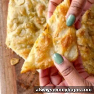 Two hands with painted nails gently holding a piece of golden-brown focaccia bread.