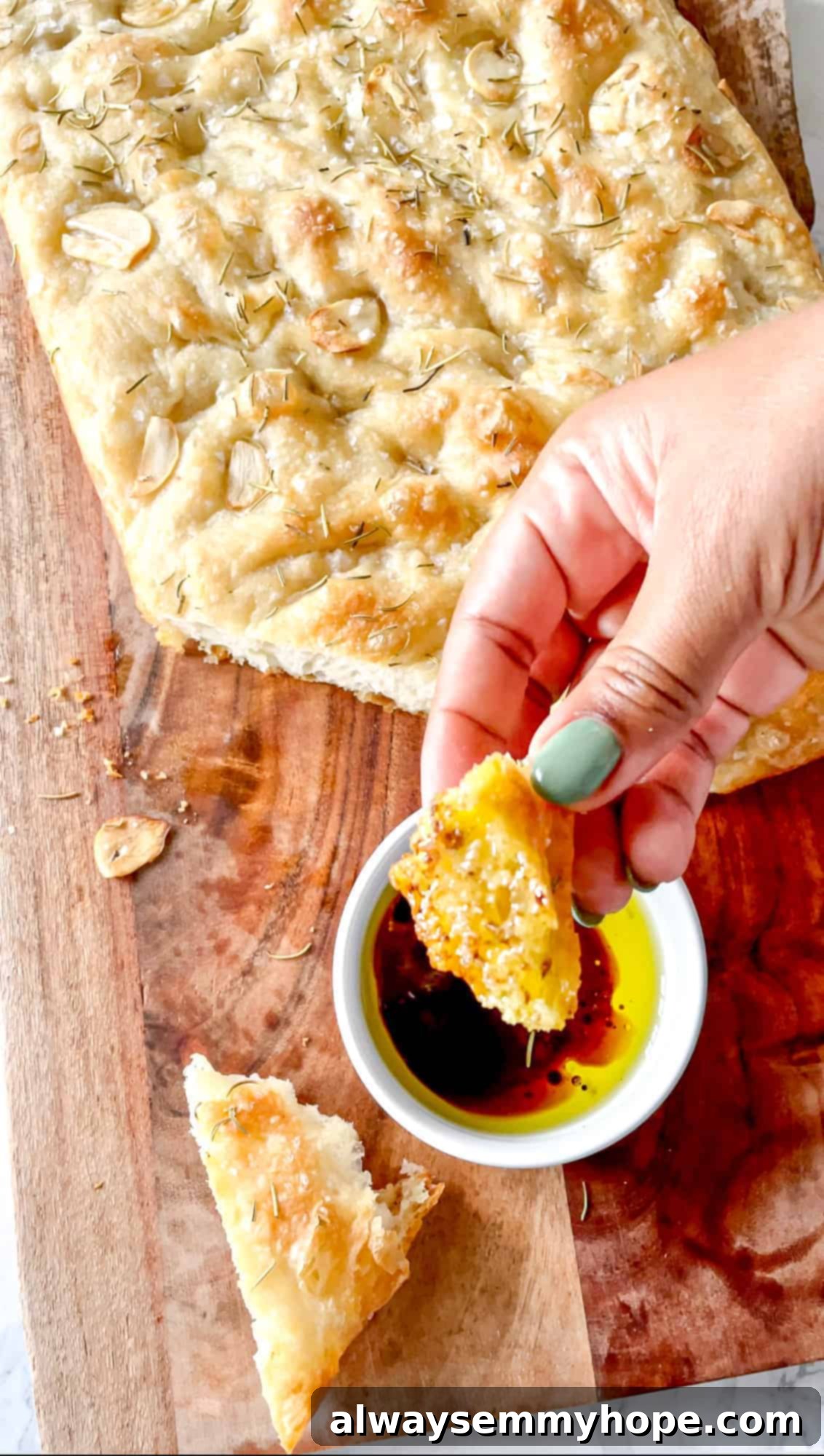 A golden-brown focaccia bread slice being dipped into a small bowl containing olive oil and balsamic vinegar, illustrating its perfect texture for dipping.