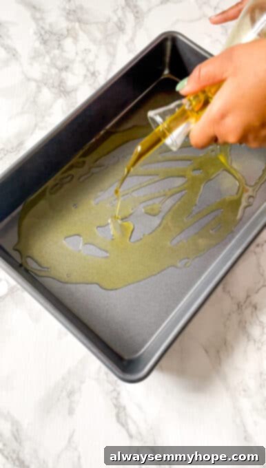 A stream of olive oil being drizzled generously into a rectangular baking dish, preparing it for the focaccia dough.