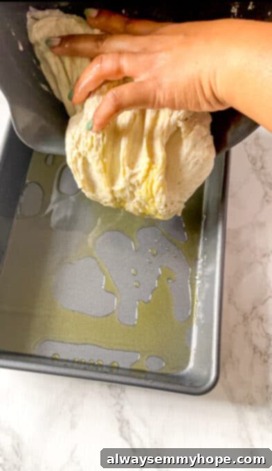 Focaccia dough being poured or gently transferred into a well-oiled rectangular baking pan.