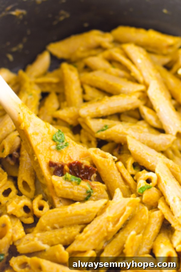 Creamy One-Pot Penne Alfredo 3 Alfredo penne pasta stirred with sun-dried tomatoes in a black pot, showcasing its creamy texture.