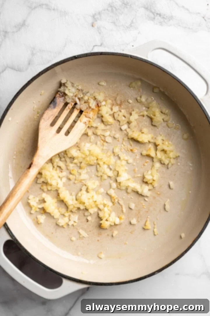Finely diced onion and minced garlic sizzling gently in a skillet with oil, beginning to soften and release their aromatic flavors.